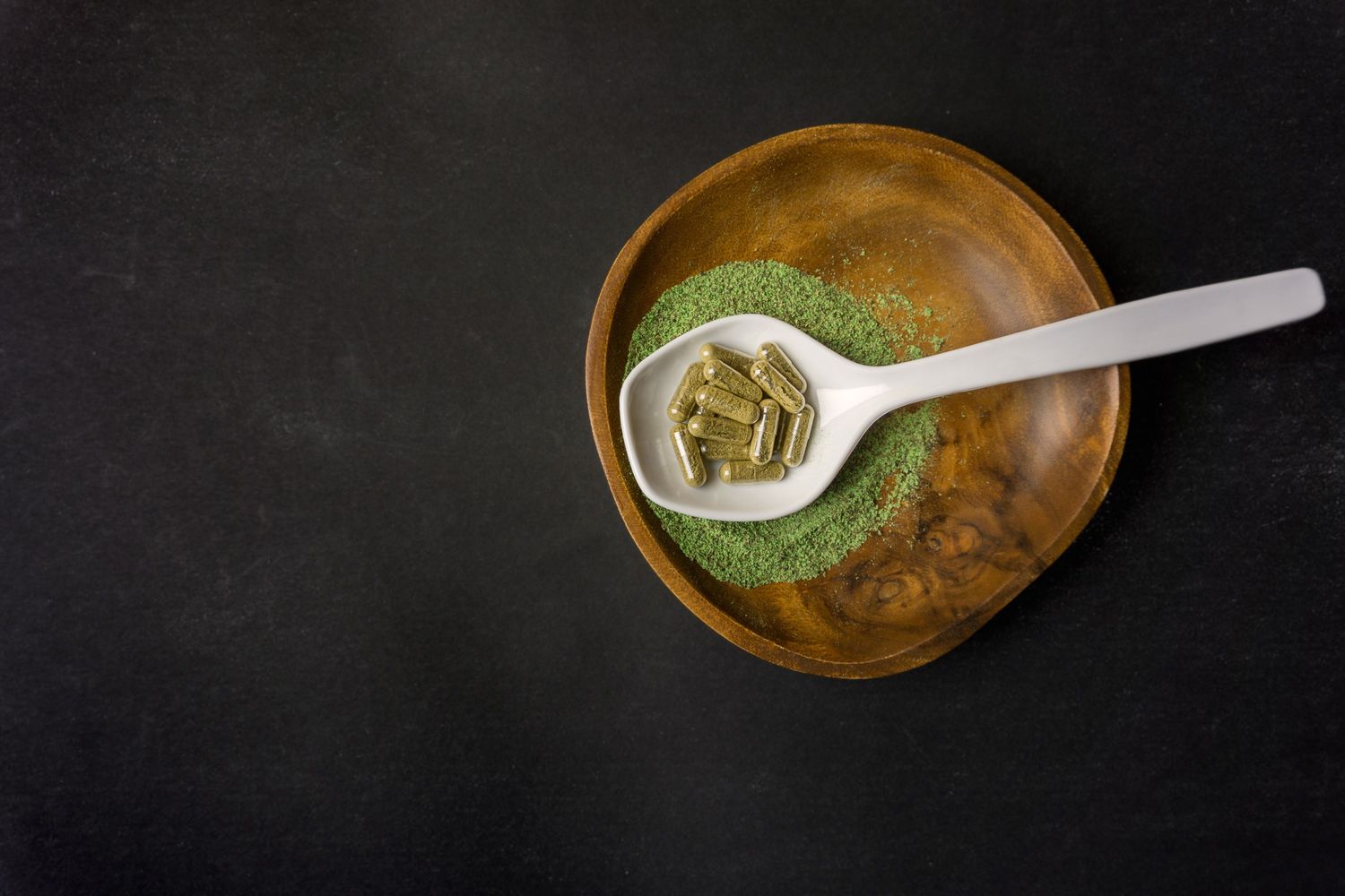 Kratom powder and capsules in a wooden bowl, available at a Tulsa kratom shop.