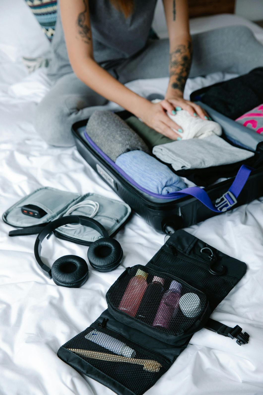 Woman packing suitcase on bed with clothes, headphones, and toiletries from Delta 8 Shop Tulsa.