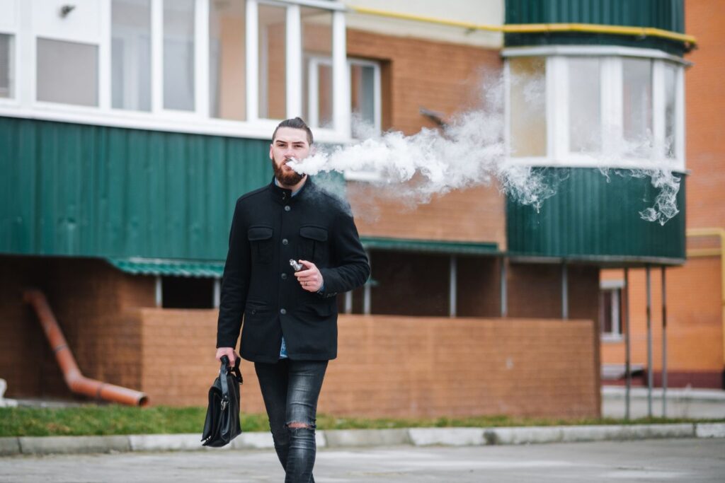 Man vaping outside with a briefcase, near a Tulsa Delta 8 shop, with vapor trail visible.