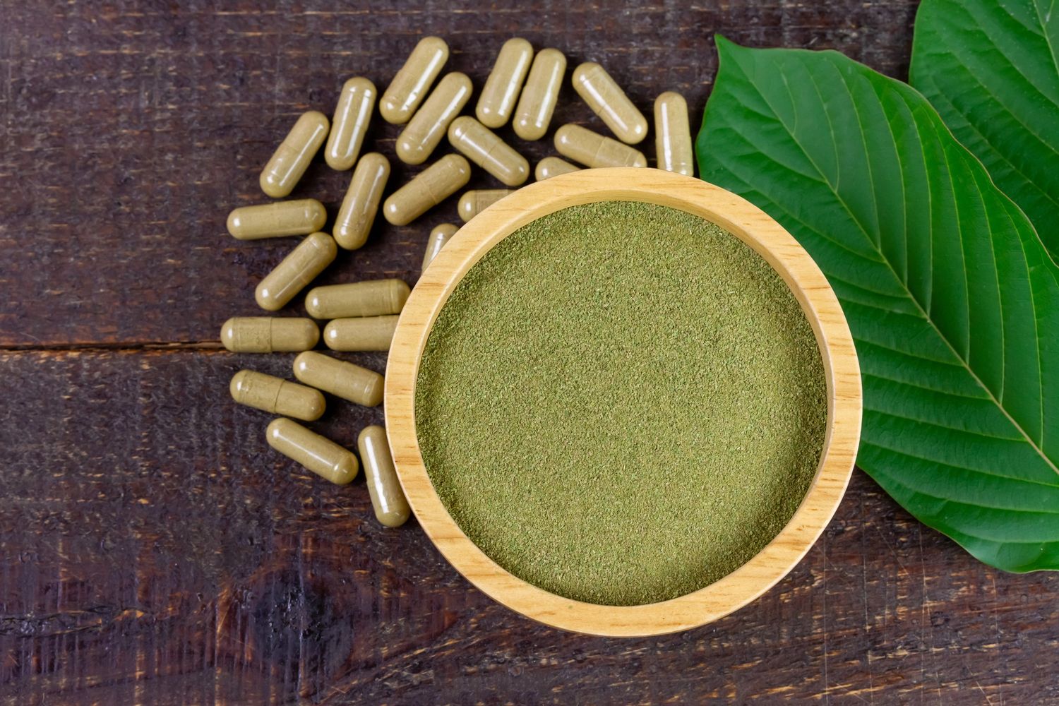Kratom powder in a wooden bowl with capsules and leaves, displayed at a Tulsa kratom retail store.