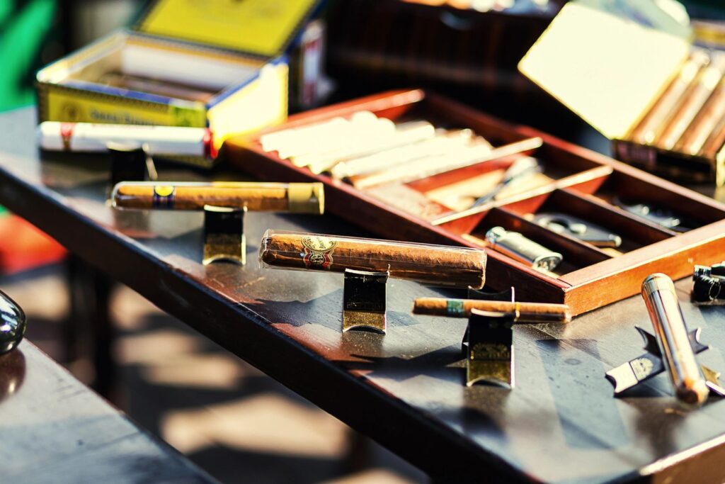 Premium cigars displayed on stands and in a wooden box at a shisha store in Tulsa, with colorful packaging in the background.