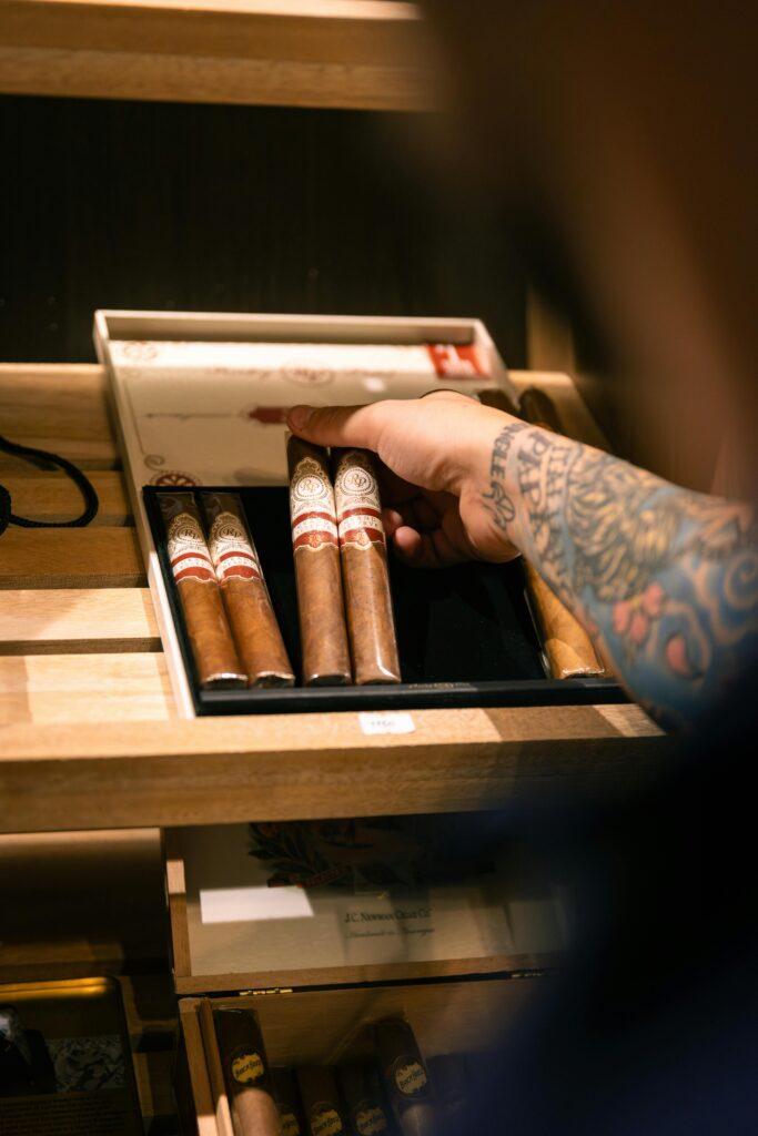 Customer's tattooed hand selecting a premium cigar for budget from the humidor at Cigar Store Tulsa.