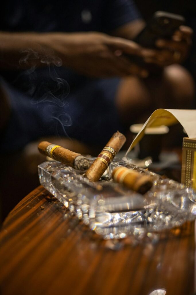 Three medium-bodied cigars resting in a crystal ashtray on a wooden table inside Cigar Store Tulsa.