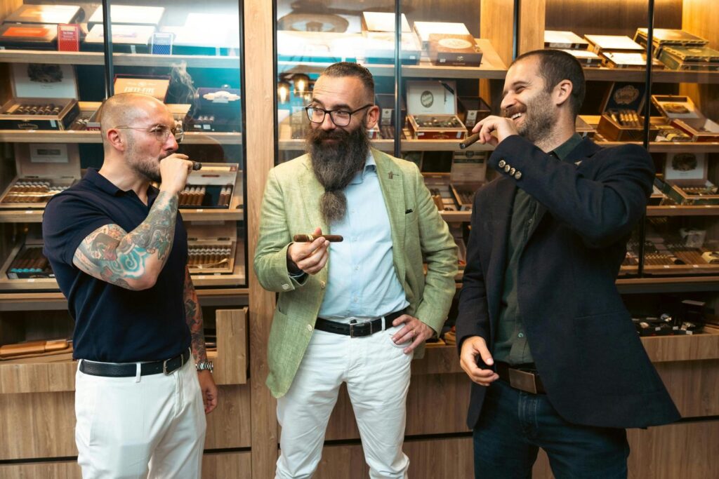 Group of stylish men enjoying premium cigars in a well-stocked Cigar Shop Tulsa, featuring tattooed enthusiast and bearded connoisseur.