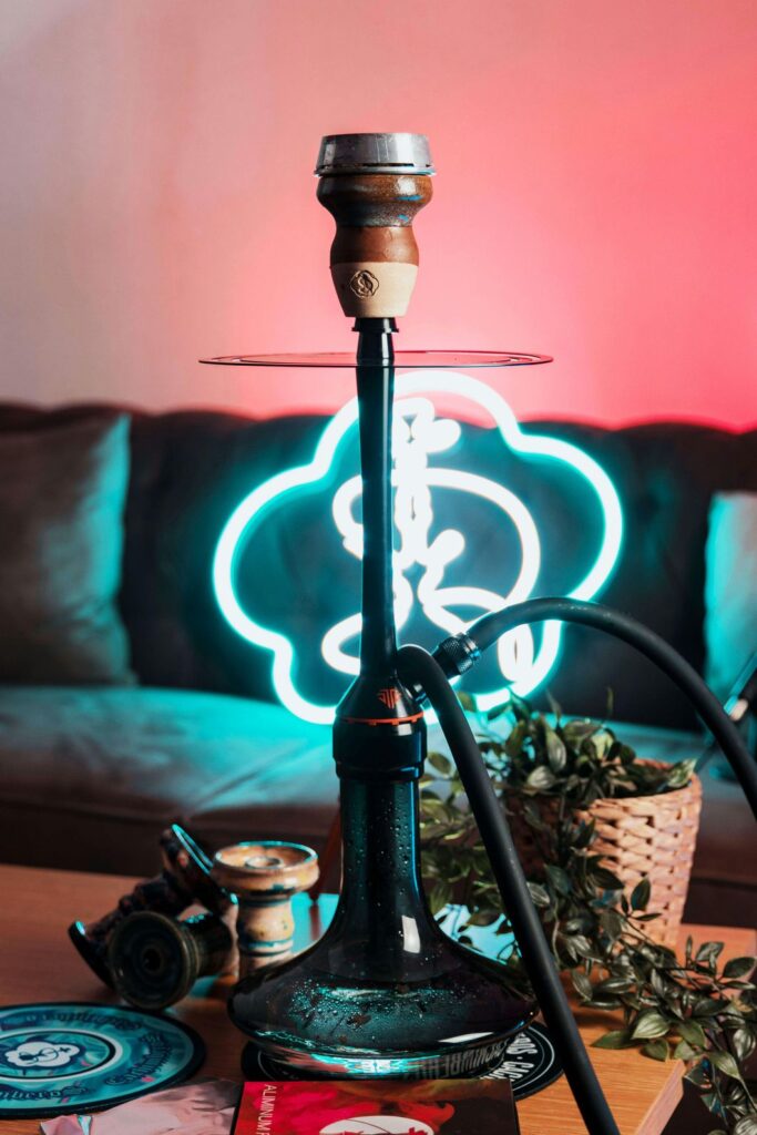 Modern black shisha setup with ceramic bowl, hose, and neon cloud sign in a lounge setting at Shisha Store Tulsa.