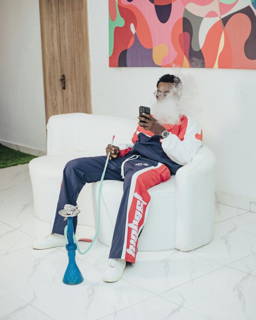 Man relaxing and vaping shisha on a white lounge chair with blue hookah pipe in a modern setting at Shisha Store Tulsa.
