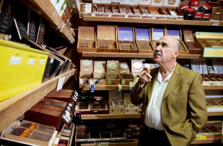 Man inspecting a cigar while browsing a wall of premium cigar boxes and humidors at a Smoke Store Tulsa.