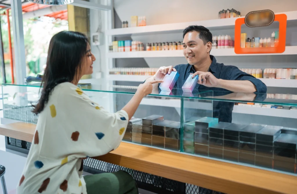 Smoke shop employee assisting a smiling customer with e-liquid or vape devices at the counter of a great Smoke Store Tulsa.