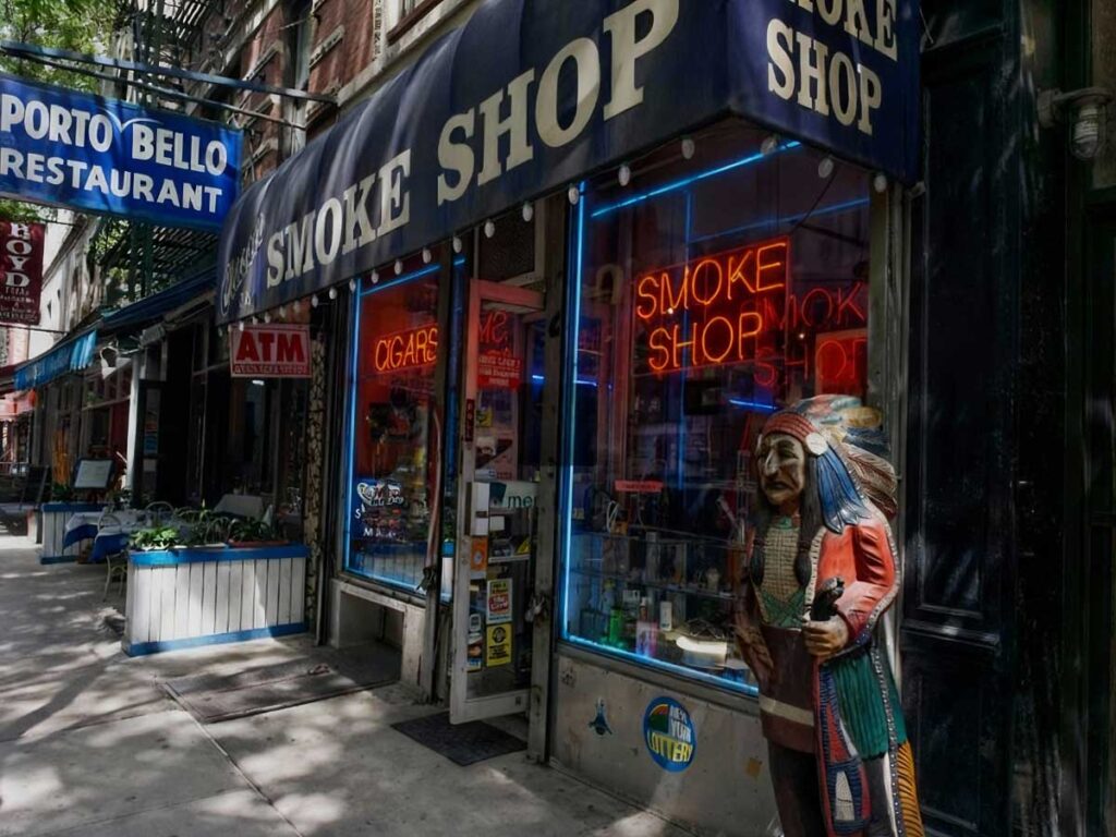 Exterior of a head shop Tulsa with neon signs and a Native American statue, offering a variety of smoking products.