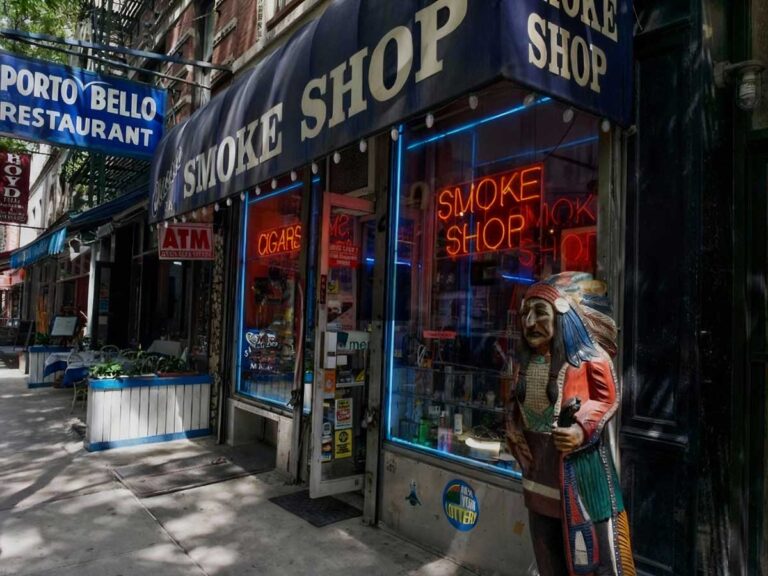 Exterior of a head shop Tulsa with neon signs and a Native American statue, offering a variety of smoking products.