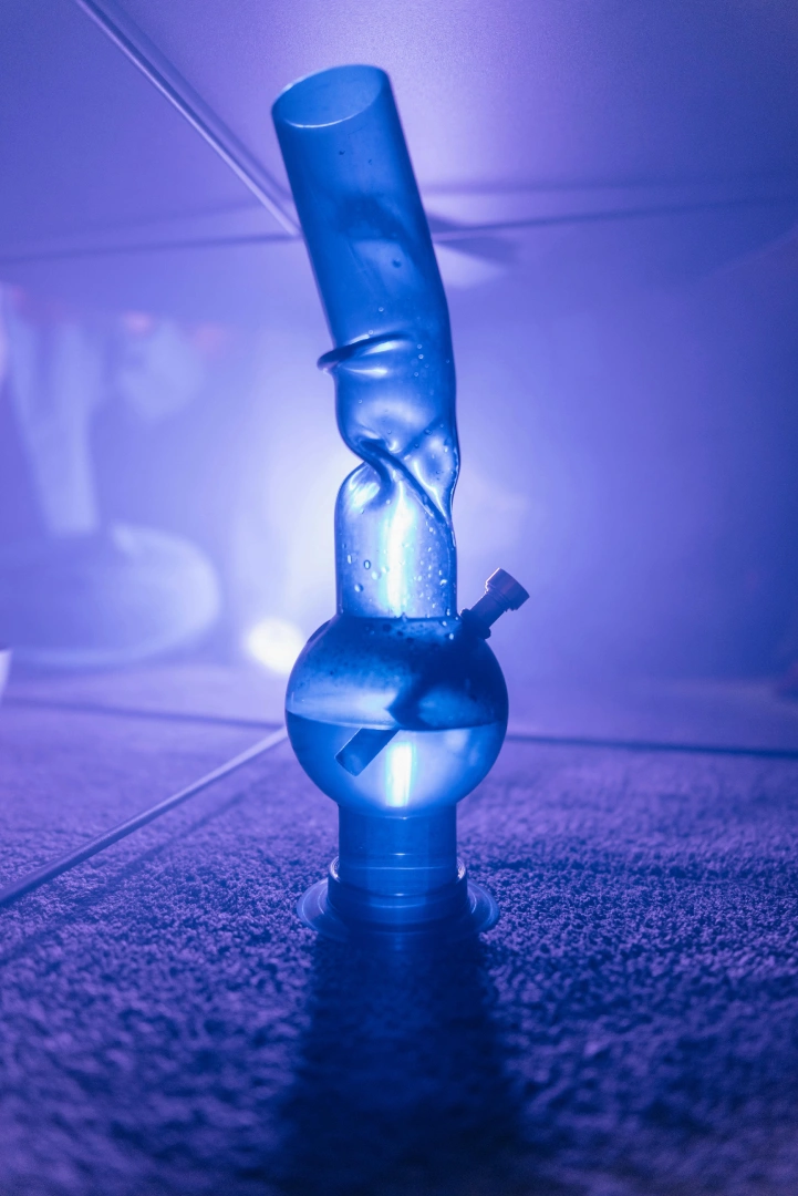 Blue-lit glass bong with water on carpeted floor, moody studio lighting for E-Cigarettes Tulsa brand product imagery