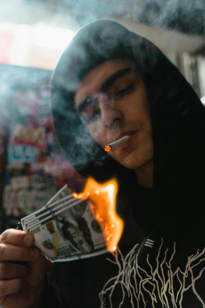Man smoking a cigarette while burning money, artistic photo illustrating smoking costs for Cigarettes shop Tulsa audience