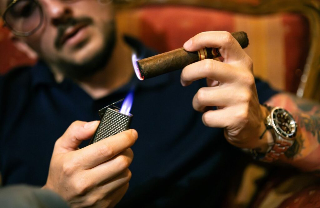 Man lighting a dark cigar with a high-flame metal lighter. Get premium cigars and tobacco supplies at Tobacco Shop Tulsa.