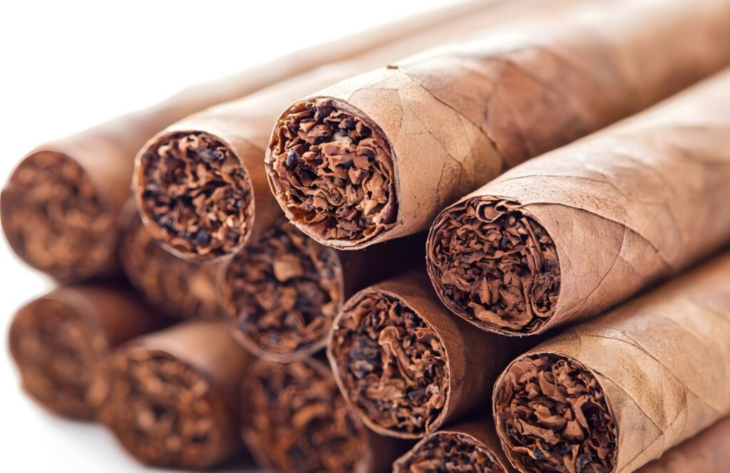 Macro shot of several wrapped cigars stacked together, showing the rich, brown tobacco filler. Shop premium cigars at Tobacco Shop Tulsa.