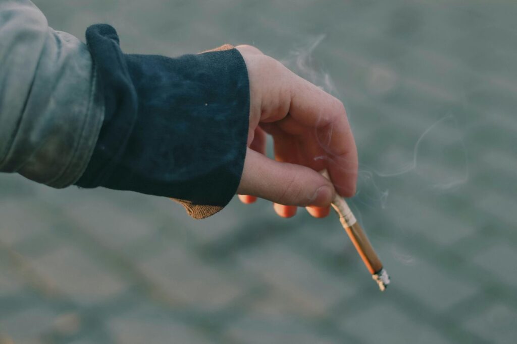 Person in a jacket lighting a tobacco cigarette outdoors. Stock up on your favorite brands at Cigarette Shop Tulsa.