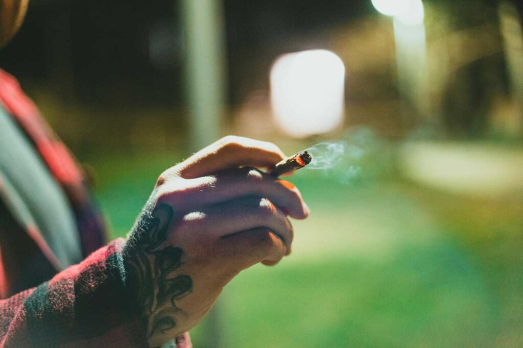 Close-up of a person holding a smoking hand-rolled cigarette. Find this item at a leading Cigarette Shop Tulsa.