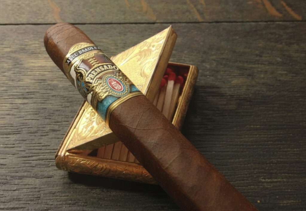 An Alec Bradley Prensado cigar resting on a gold matchbox at a cigar shop Tulsa, perfect for luxury enthusiasts.
