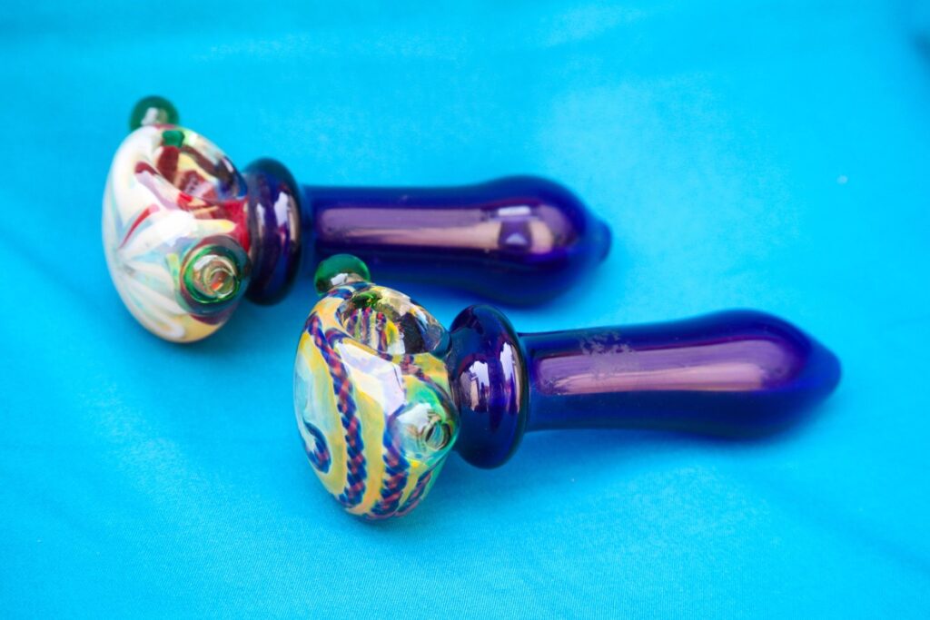 Two cobalt blue glass pipes Tulsa spoon style featuring vibrant multicolored artistic swirls on the bowl head.