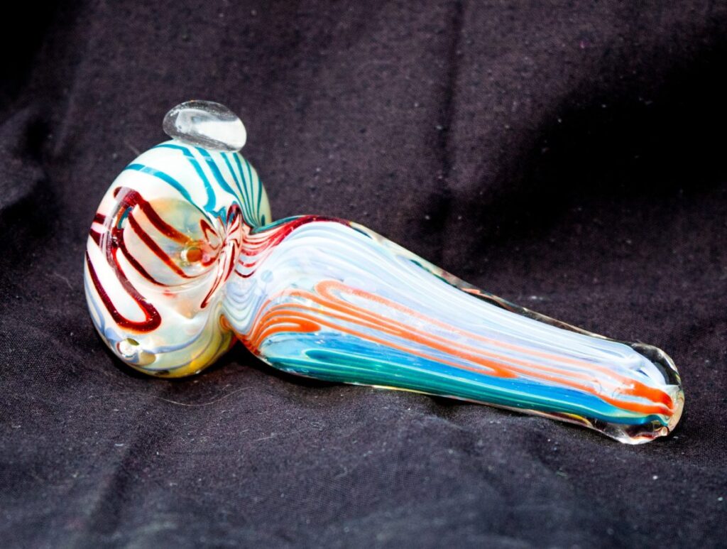 A colorful swirl glass pipes Tulsa spoon pipe with red blue and orange patterns on a textured black background.