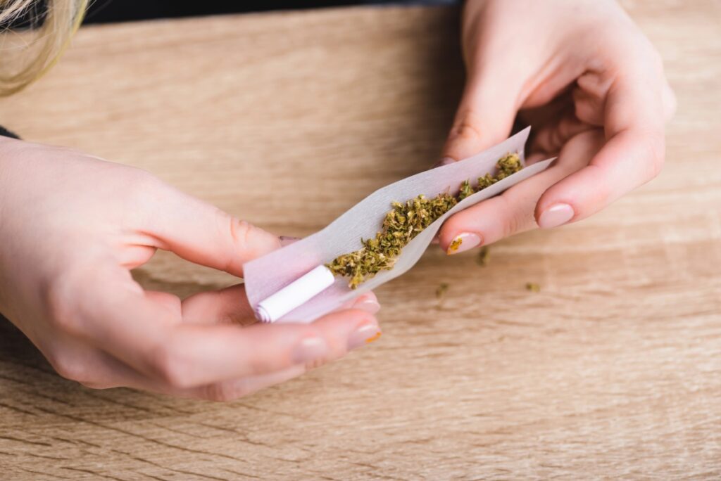 Person using high-quality rolling papers Tulsa dispensaries provide to hand-roll medical cannabis on a wood table.