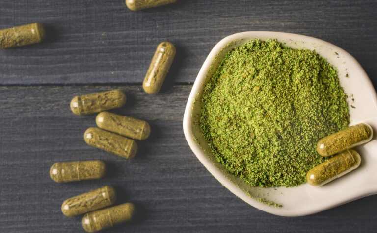 Green vein capsules and loose herbal powder on a white ceramic spoon, available at your local kratom shop Tulsa.