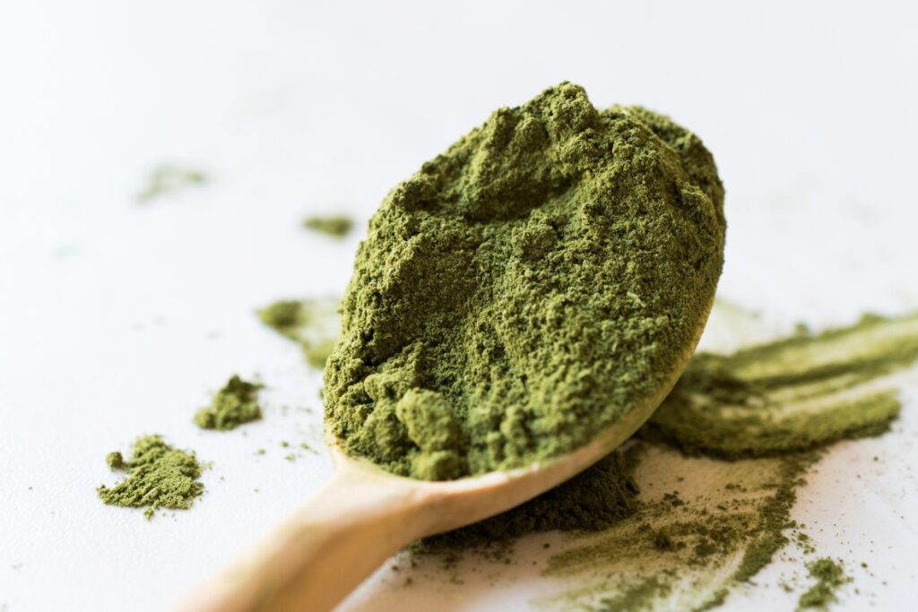 Premium green powder on a wooden spoon at a kratom shop Tulsa, showing the fine texture and quality of the herb.