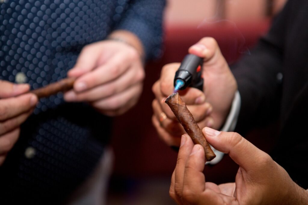 A gentleman in a dark suit expertly uses a torch lighter to ignite a fine cigar at a cigar shop Tulsa.