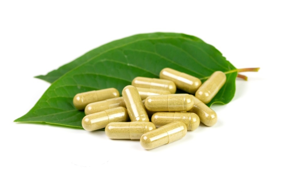 A cluster of premium herbal capsules resting on fresh green leaves, available online or at our kratom shop tulsa.