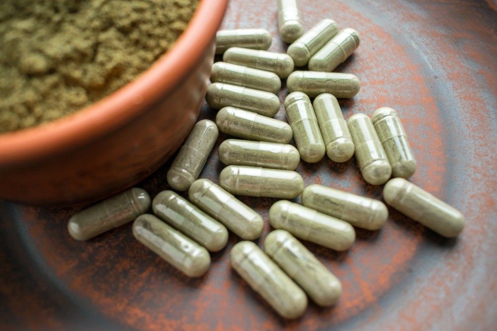 A detailed shot of premium green herbal powder and transparent capsules, perfect for finding at our kratom shop tulsa location.
