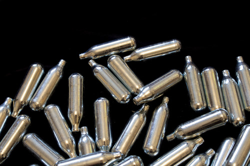 Scattered silver nitrous oxide chargers Tulsa on a dark background for retail culinary supplies and cream whipping.