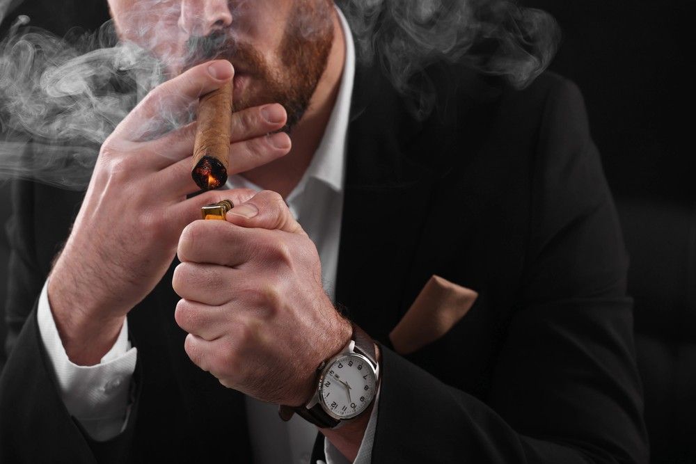Premium cigar shop Tulsa experience featuring a man in a suit lighting a luxury hand-rolled cigar with a lighter.