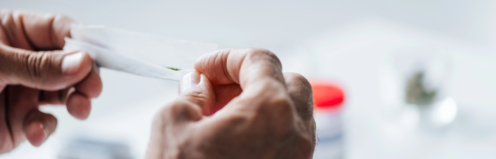 Close-up on skilled hands carefully rolling a paper with green herb, showing the craft from our head shop Tulsa.