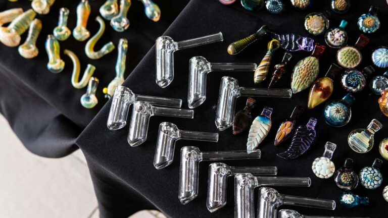 Top-down view of artistic glass bangers, pipes, and detailed pendants on a black cloth, a unique selection at head shop Tulsa.