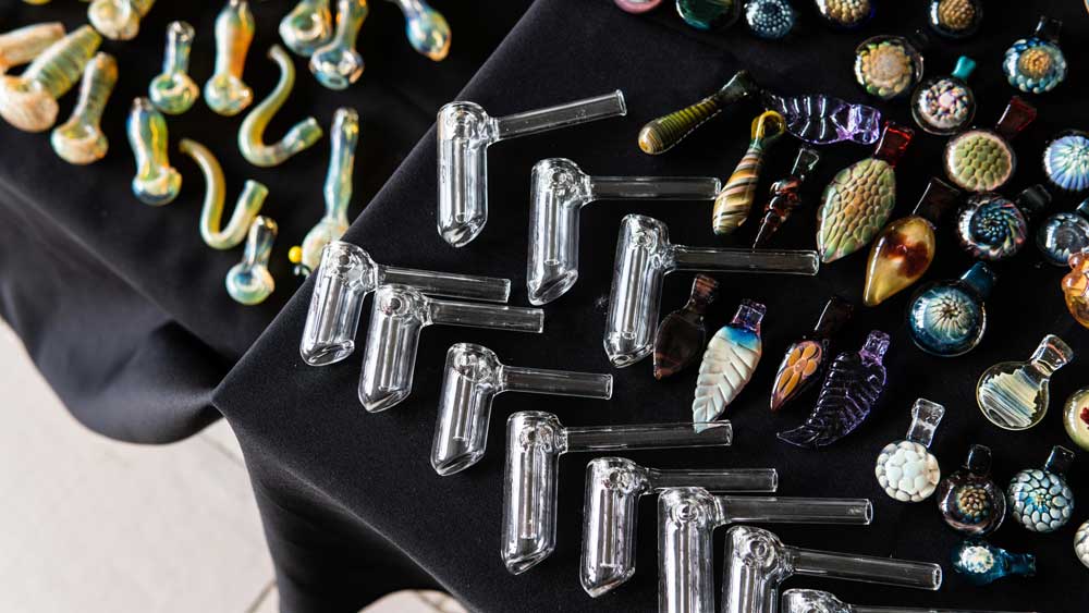 Top-down view of artistic glass bangers, pipes, and detailed pendants on a black cloth, a unique selection at head shop Tulsa.