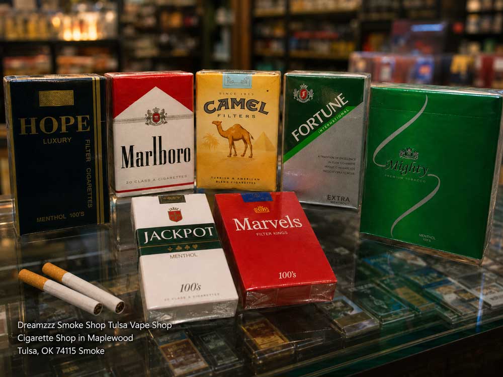 Popular cigarette packs like Marlboro and Camel displayed on a glass counter at a cigarette shop Tulsa store